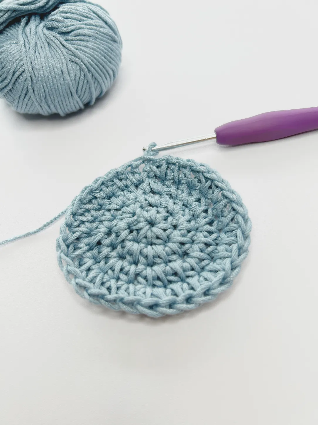 flat crochet circle on table and blue yarn and purple crochet hook